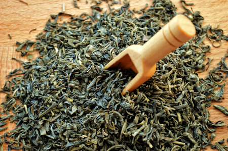 Wooden spoon lies in a heap of loose tea on a wooden background