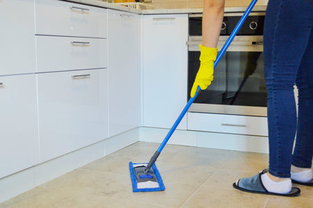 Young woman washing mop the tiled floor in the kitchen