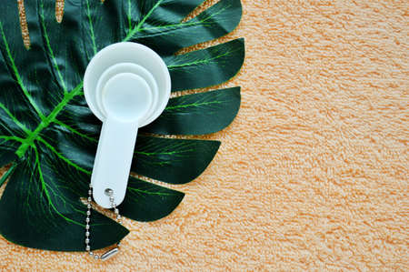 White plastic measuring spoons lie on a palm leaf on a beige cloth background.の写真素材