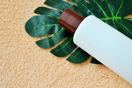 White plastic bottle lies on a palm leaf on a beige cloth background