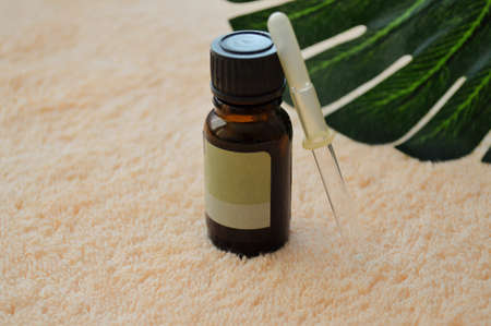 Glass jar and pipette lie on a palm leaf on a beige cloth background.の写真素材