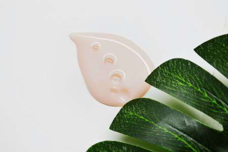 Pink drop of cosmetic product with bubbles on white background with green palm leafの写真素材