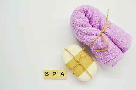 White soap tied with rope and brown paper and pink towel lies on a white background. word Spa made of wooden lettersの写真素材