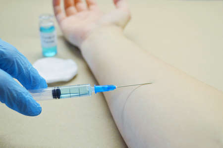 Doctor's hand injects a vaccine into the patient's hand against the background of a glass jar with a vaccineの写真素材