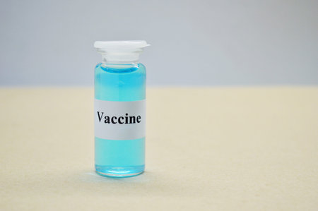 Glass jar with liquid blue vaccine on light background.