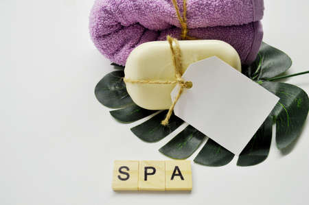 White soap with a label and pink towel lies on a white background lies on a green leaf of a palm tree. word Spa made of wooden lettersの写真素材