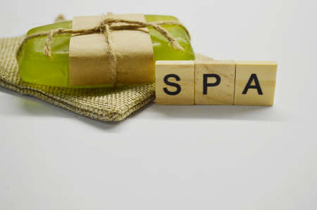 Green soap tied with rope and brown paper lies on a white background on a jute bag. word Spa made of wooden lettersの写真素材