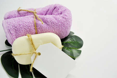 White soap with a label and pink towel lies on a white background lies on a green leaf of a palm tree.の写真素材