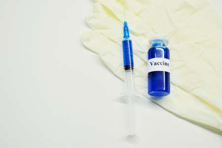 Glass jar with liquid blue vaccine, syringe and white rubber gloves on light background.の写真素材