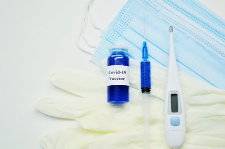 Glass jar with liquid blue vaccine, syringe, electronic thermometer, white rubber gloves and medical...