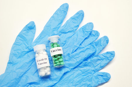 Glass jars with vaccine and blue rubber gloves on a light background.