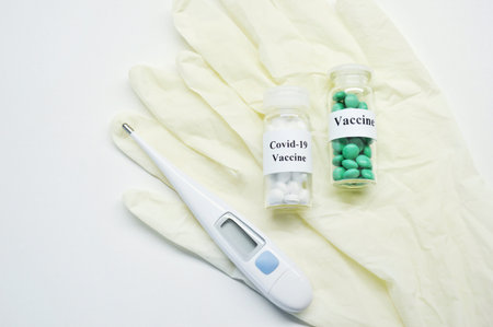 Glass jars with vaccine, electronic thermometer and white rubber gloves on a light background