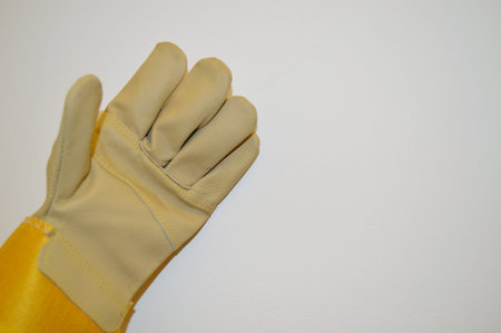 Beige and yellow work cloth glove against a white wall background.