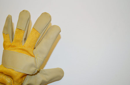 Beige and yellow work cloth glove against a white wall background.の写真素材