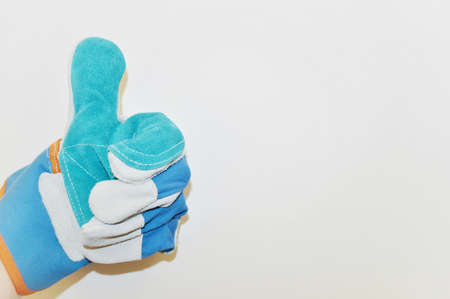 Hand in blue work cloth glove shows sign class against white wall backgroundの写真素材