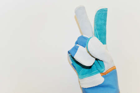 Hand in blue work cloth glove shows two thumbs up against white wall backgroundの写真素材