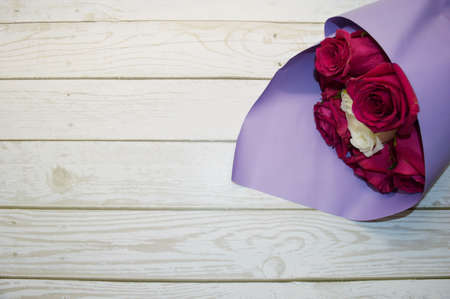 Bouquet of red roses in purple packaging lies on white wooden background.の写真素材