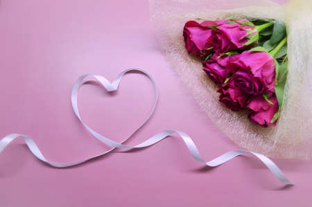 Bouquet of red roses lies on pink background. Heart made from white ribbonの写真素材