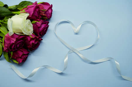 Bouquet of red roses lies on a blue background. Heart made from white ribbonの写真素材