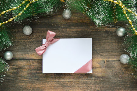 Blank white postcard with pink ribbon on dark wooden background with fir branches and silver Christmas balls. Catholic Christmas Ever. Christmas Card Day. New Yearの写真素材