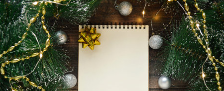 Blank white notebook with yellow bow on dark wooden background with fir branches and silver...