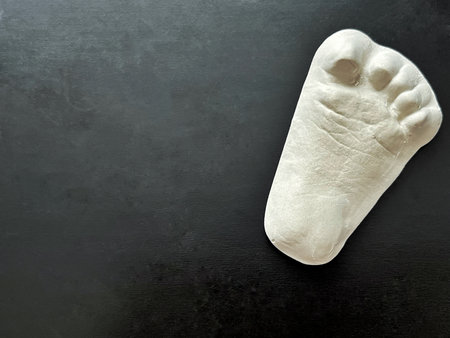 White plaster footprint sculpture rests on dark textured surface, highlighting craftsmanship and artistic detail, creating a striking visual contrast and minimalist aestheticの写真素材