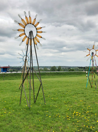 Unique wind sculptures are prominently displayed in a lush green field, surrounded by a cloudy sky,...