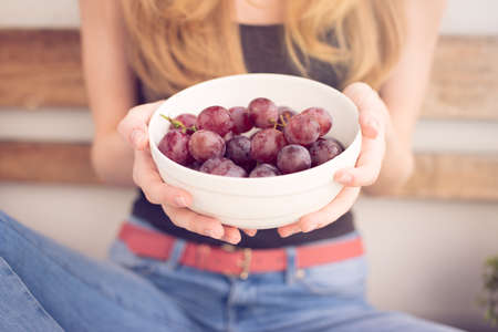 Girl is holding with two hands a bowl of grape (sunset)の写真素材