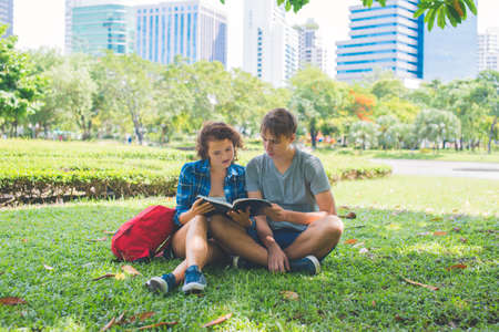 Students reading a book and sitting in the parkの写真素材
