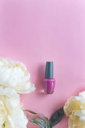 Pink nail polish on the pink background with flowers aroundの写真素材