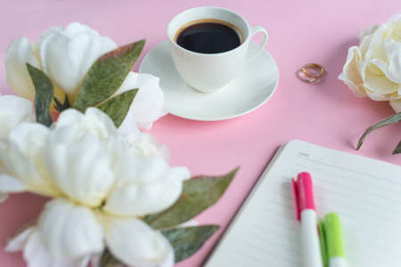 A cup of coffee and notebook on the pink background with white peony. Planning.の写真素材