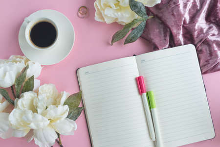 A cup of coffee and notebook on the pink background with flowersの写真素材