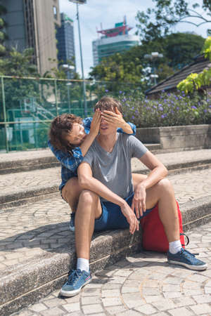 Young girl close eyes of her friend with hands. Sitting on the stairs. Summerの写真素材