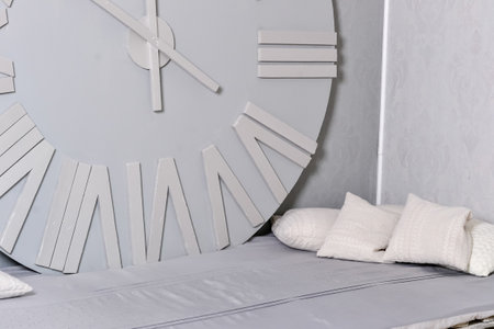 White clock on a white wall. Wall clock on white background, front view. Interior decoration. White pillows on the sofa. Cristmas time. Wall clock. Interior decoration. High quality photoの写真素材
