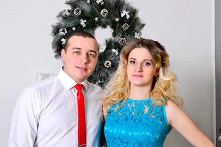 Attractive young couple is celebrating holiday at home. Standing on the background of beautiful Christmas tree husband hugs his pregnant wife. A man and his pregnant wife stand by a Christmas tree. High quality photoの写真素材