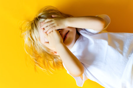 The kid is 2 years old with blonde hair, dressed in a white T-shirt and yellow pants on a yellow background. Emotions. The concept of childhood and family. Baby front view yellow isolated background with a happy and excited expressionの写真素材