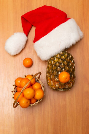 New Years composition is on a wooden background. New Years hat, pineapple and tangerines. Santas hat. Christmas conceptの写真素材