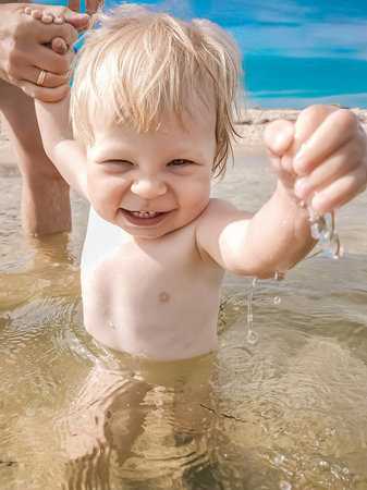 Kid in the sea holding fathers hand. Happy child playing in the sea. Kid having fun outdoors. Summer vacation and healthy lifestyle concept. Trust family concept.の写真素材