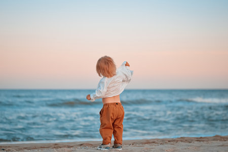 Happy child child wearing a white shirt next to the sea going next to the sea. Place for text. Copy space. Happy child going in the beach Kid having fun outdoors. Summer vacation and healthy lifestyle concept.の写真素材