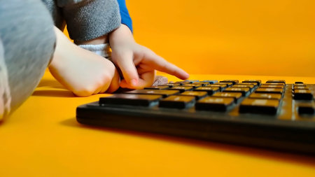 A small child counts on a calculator on a yellow background. Kid fingers press buttons and calculate studying math at home. Child makes arithmetic calculations with a calculatorの写真素材