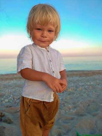Happy child child wearing a white shirt next to the sea going next to the sea. Place for text. Copy space. Happy child going in the beach Kid having fun outdoors. Summer vacation and healthy lifestyle concept.の写真素材