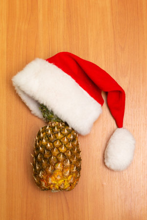 New Years composition is on a wooden background. New Years hat, pineapple and tangerines. Santas hat. Christmas conceptの写真素材