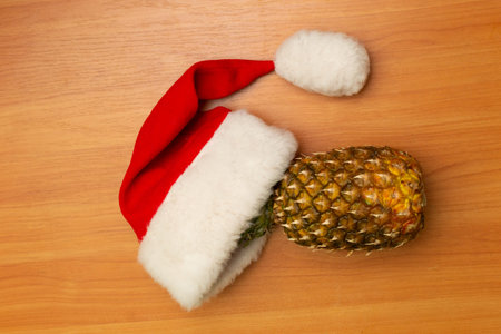 New Years composition is on a wooden background. New Years hat, pineapple and tangerines. Santas hat. Christmas conceptの写真素材
