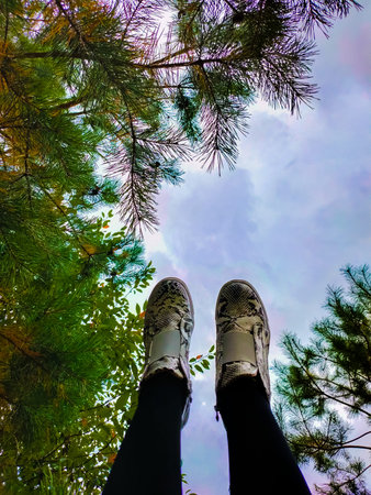 Feet in autumn shoes, in black and white boots against the sky and trees. Legs of woman in shoes...