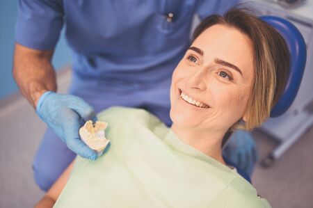 Dentist examining a patient's teeth using dental equipment in dentistry office. Stomatology and health care concept. Young handsome male doctor in disposable medical facial mask, smiling happy woman.の写真素材