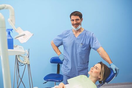 Dentist examining a patients teeth using dental equipment in dentistry office. Stomatology and health concept. Young handsome male doctor in disposable medical facial mask, smiling happy woman.の写真素材