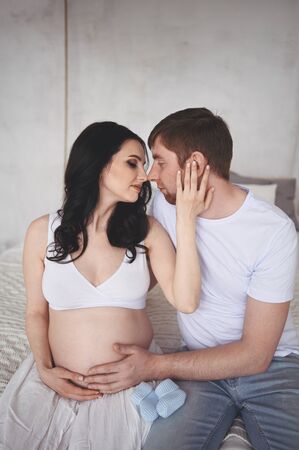 Pregnancy and people concept - happy man hugging his beautiful pregnant wife at home. Future parents waiting unborn baby. Love, relationship, birth, happy family concept - young lovely married coupleの写真素材