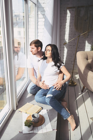 Pregnancy and people concept - happy man hugging his beautiful pregnant wife at home. Future parents...