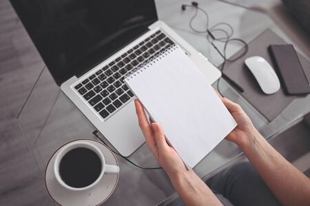Unrecognizable woman hands writing in empty mock up notebook and computer. Freelancer using smart phone and laptop at home during quarantine. Internet marketing, finance, business, remote work conceptの写真素材