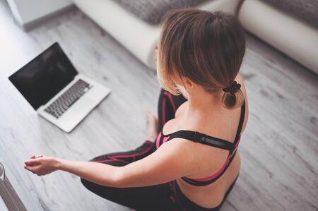 Fit young woman in sportswear practicing doing yoga exercises and watching videos online tutorials on laptop, training in living room during quarantine and closed gyms. Staying fit and healthyの写真素材